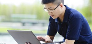 Asian-male-college-student-sitting-and-looking-at-an-open-laptop